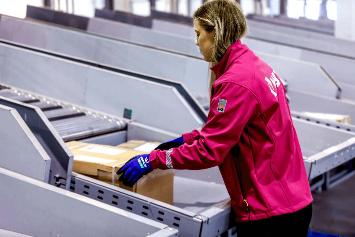 Fotografi av en lageransatt, med NBT-uniform. Hun sorterer pakker.